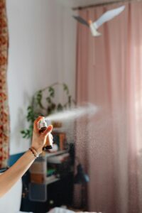 A woman's hand spraying fragrance in a cozy domestic room with elegant curtains.